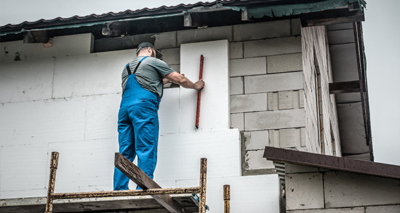 man wearing blue overalls applying insulation boards to a building wall using a straightedge during exterior renovation project 10 tips for insulation